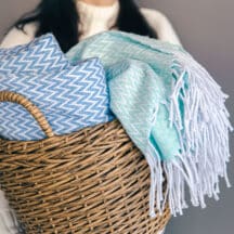 Folded blankets stood on edge in a woven basket, each one visible without unstacking the pile