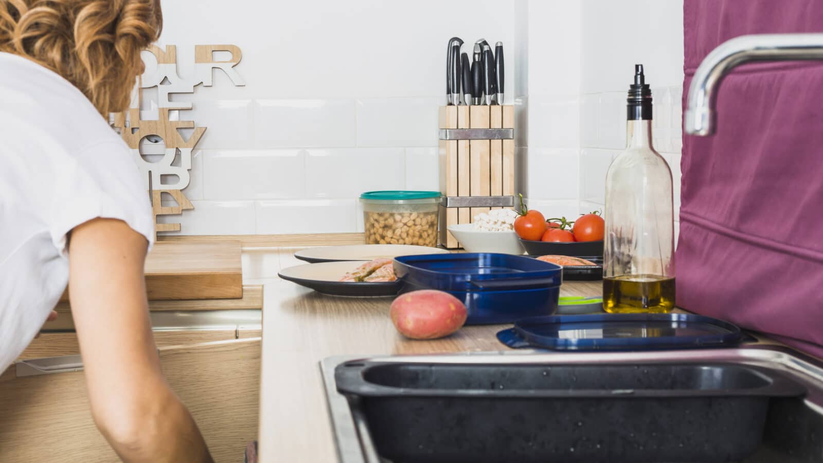 Woman opening the under-sink kitchen cabinet to organize storage around the pipes
