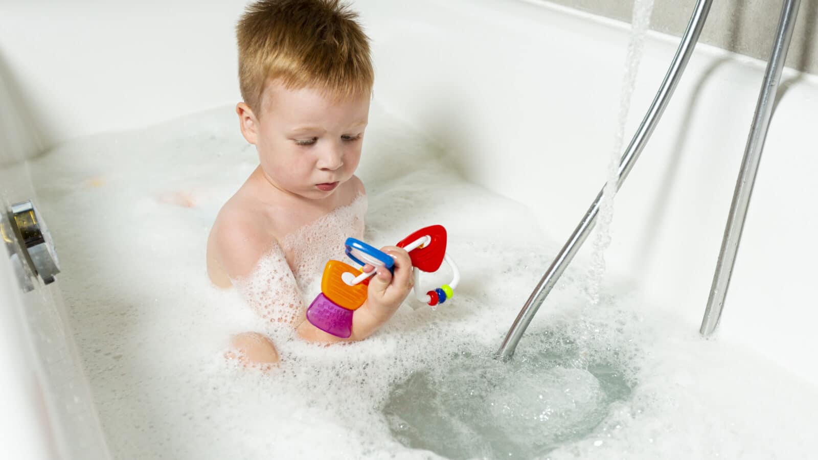 Kid playing with bath toys in the tub, an example of the toys that need to drain and dry between baths in a kids bathroom