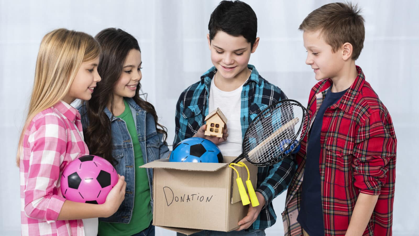 Two kids holding a donation box full of toys and clothes to declutter