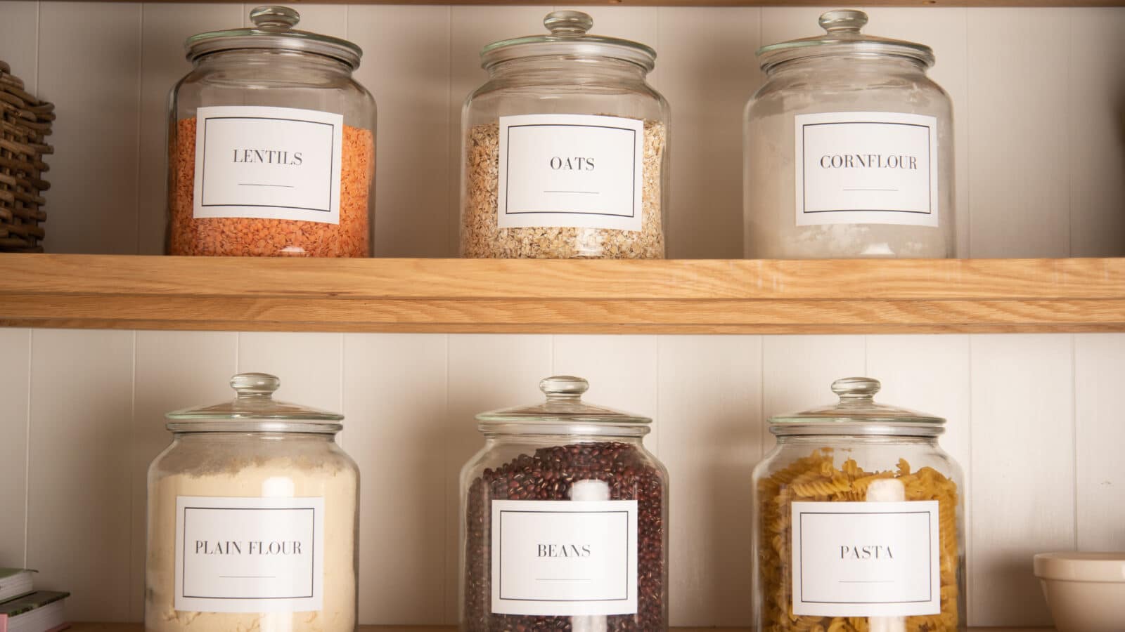 Bocaux en verre étiquetés avec pâtes, légumineuses et céréales rangés sur une étagère de garde-manger