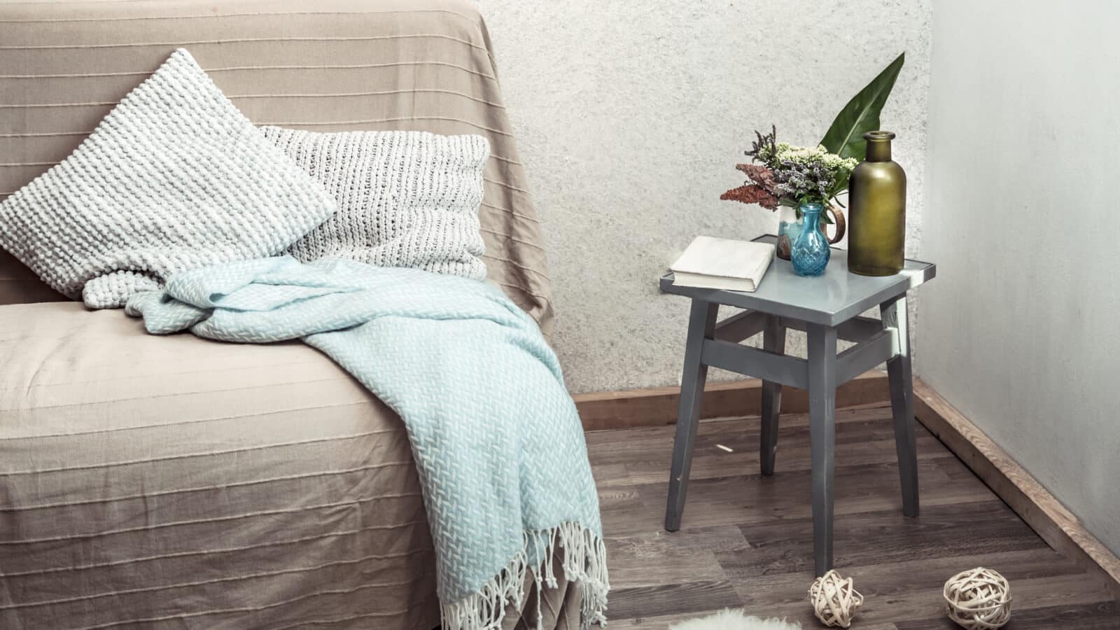 Panier en osier avec plaid et coussins près d'un canapé dans un salon