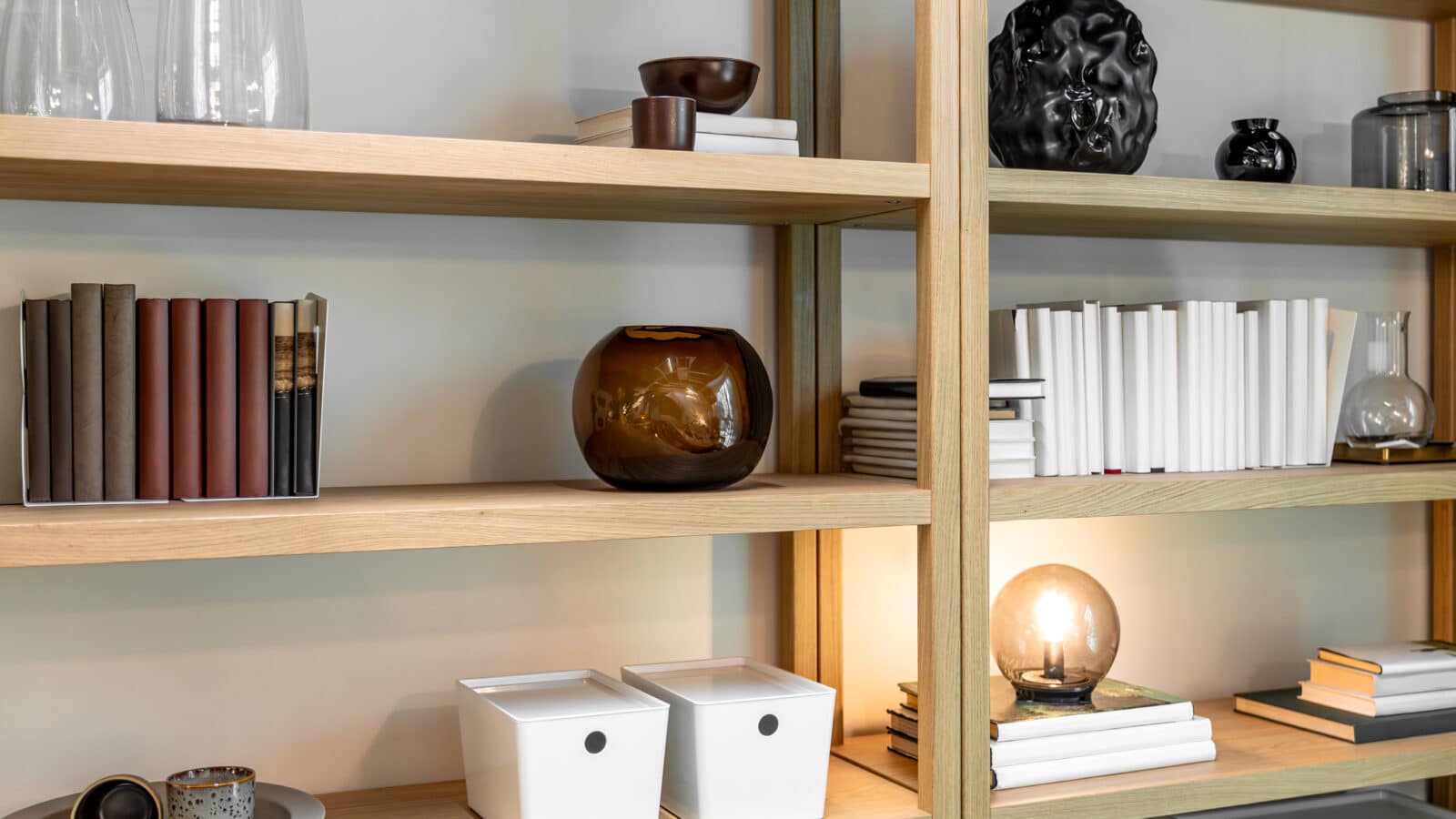 Minimal freestanding shelving unit with books and warm lamp light in a rented living room