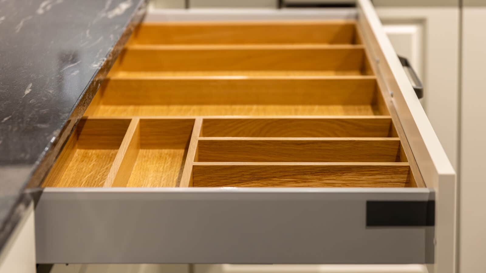 Organized kitchen drawer with wooden cutlery dividers holding utensils neatly