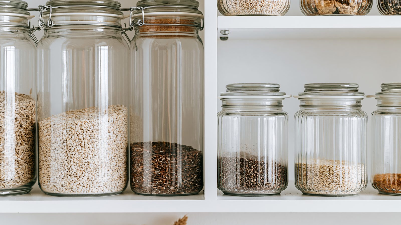 Bocaux en verre remplis de céréales et de graines rangés sur des étagères de garde-manger