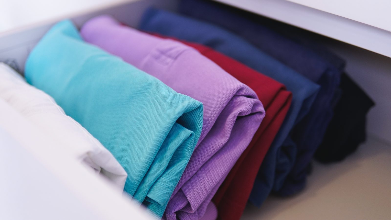 Neatly folded colorful clothes stacked on a closet shelf under soft lighting