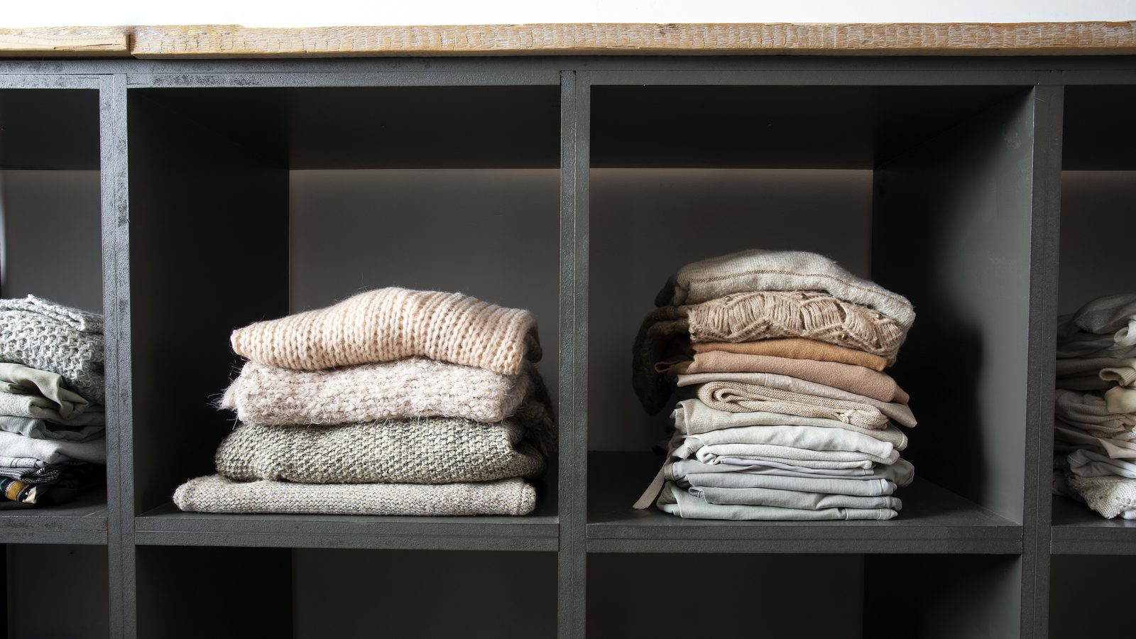 Open wardrobe shelves with neatly folded stacks of clothes and linens