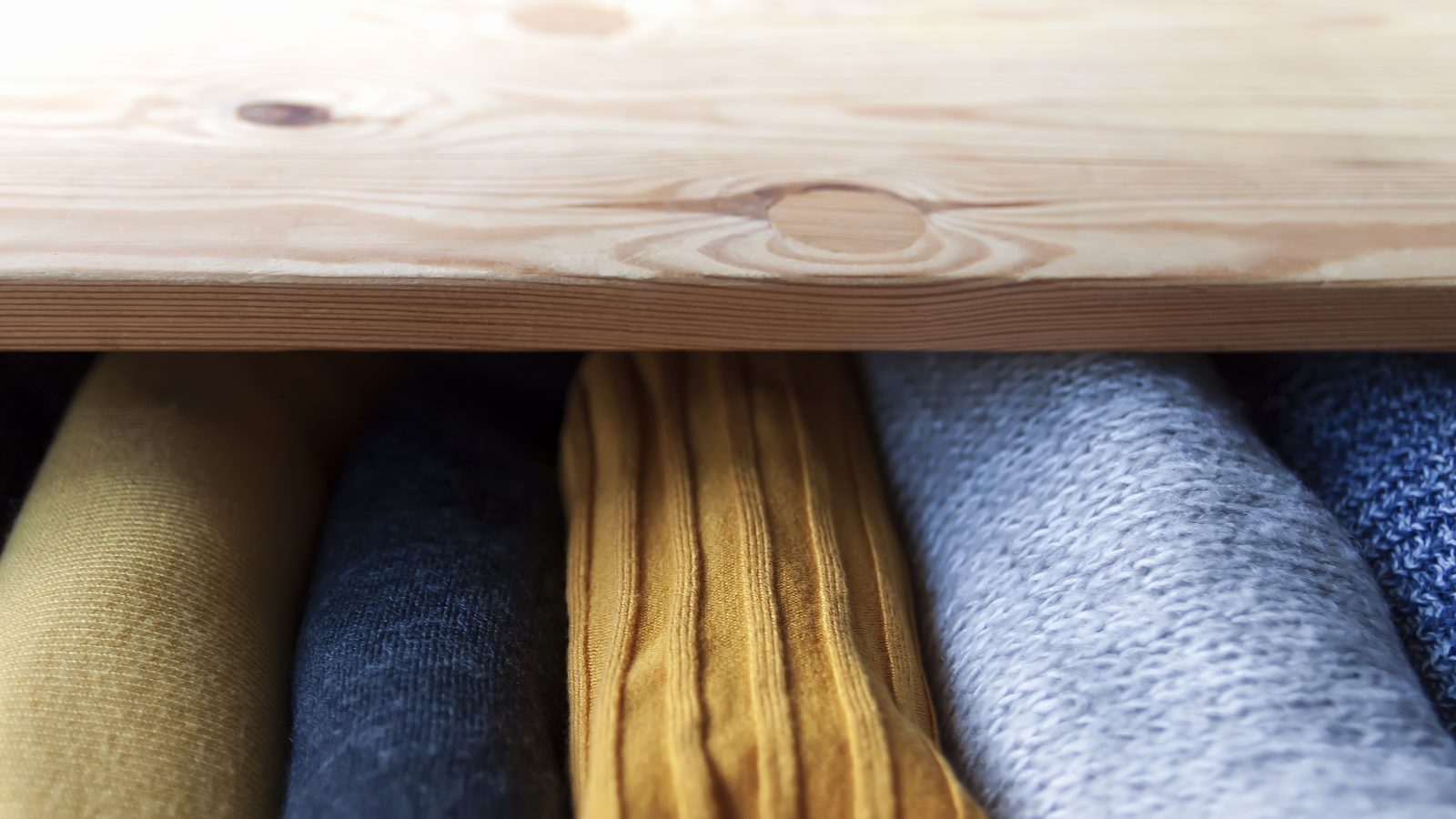 Open dresser drawer with neatly folded knitted clothes, part of a labeled storage zone assigned to one child in a shared kids bedroom