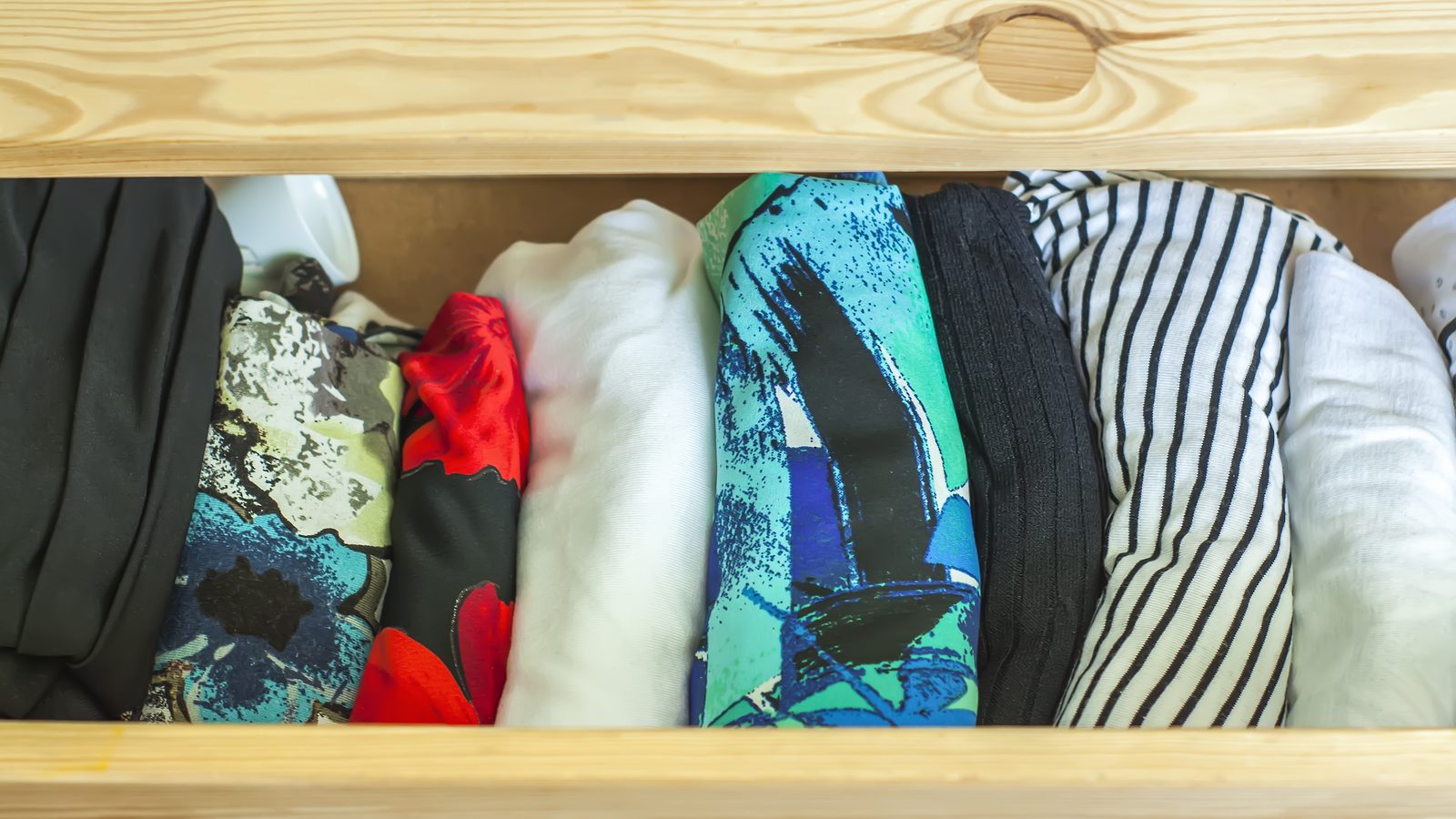 Tiroir de commode en bois clair ouvert avec des vêtements pliés et colorés bien rangés