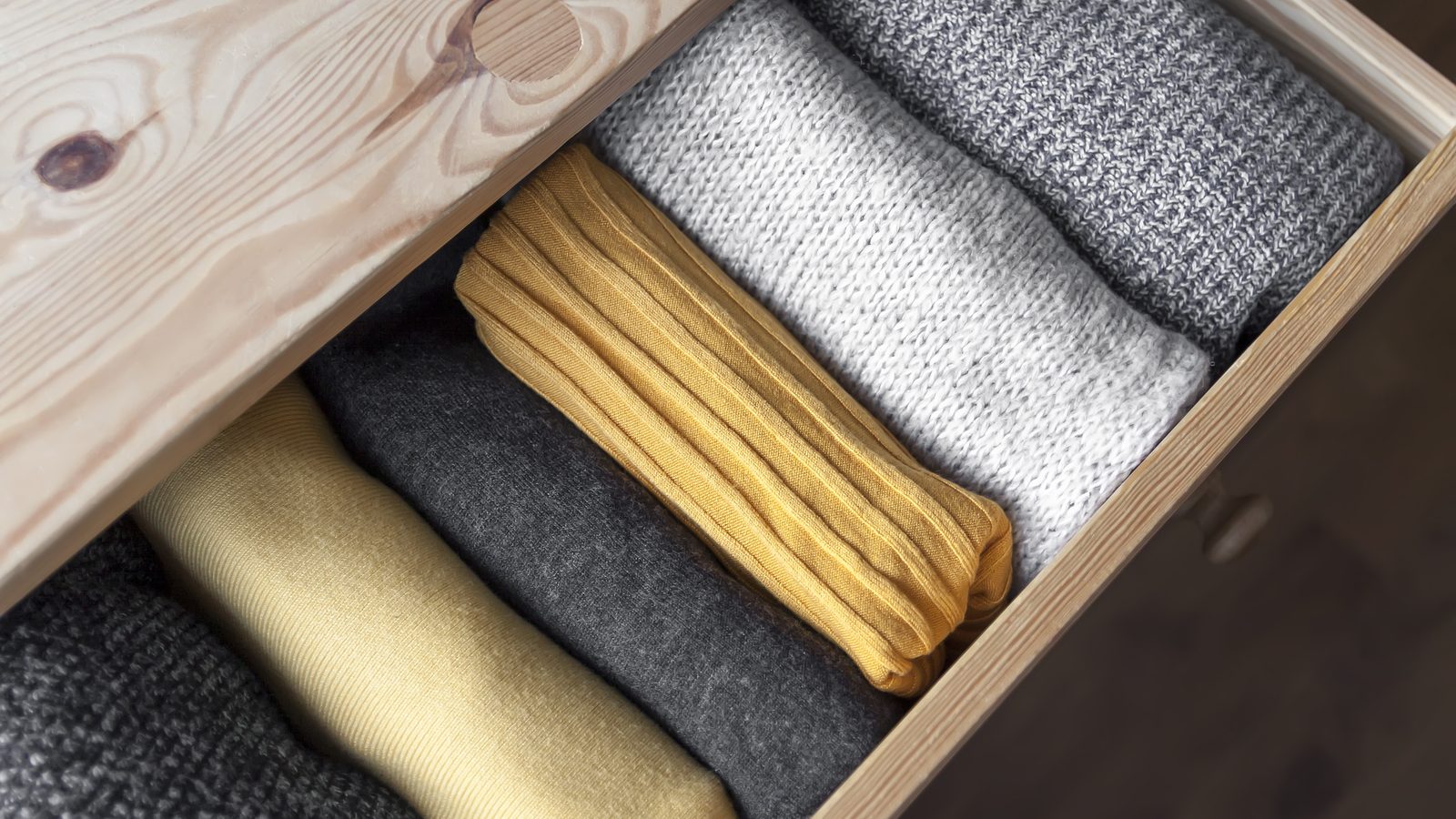 Tiroir de commode en bois ouvert rempli de vêtements en laine tricotée bien rangés