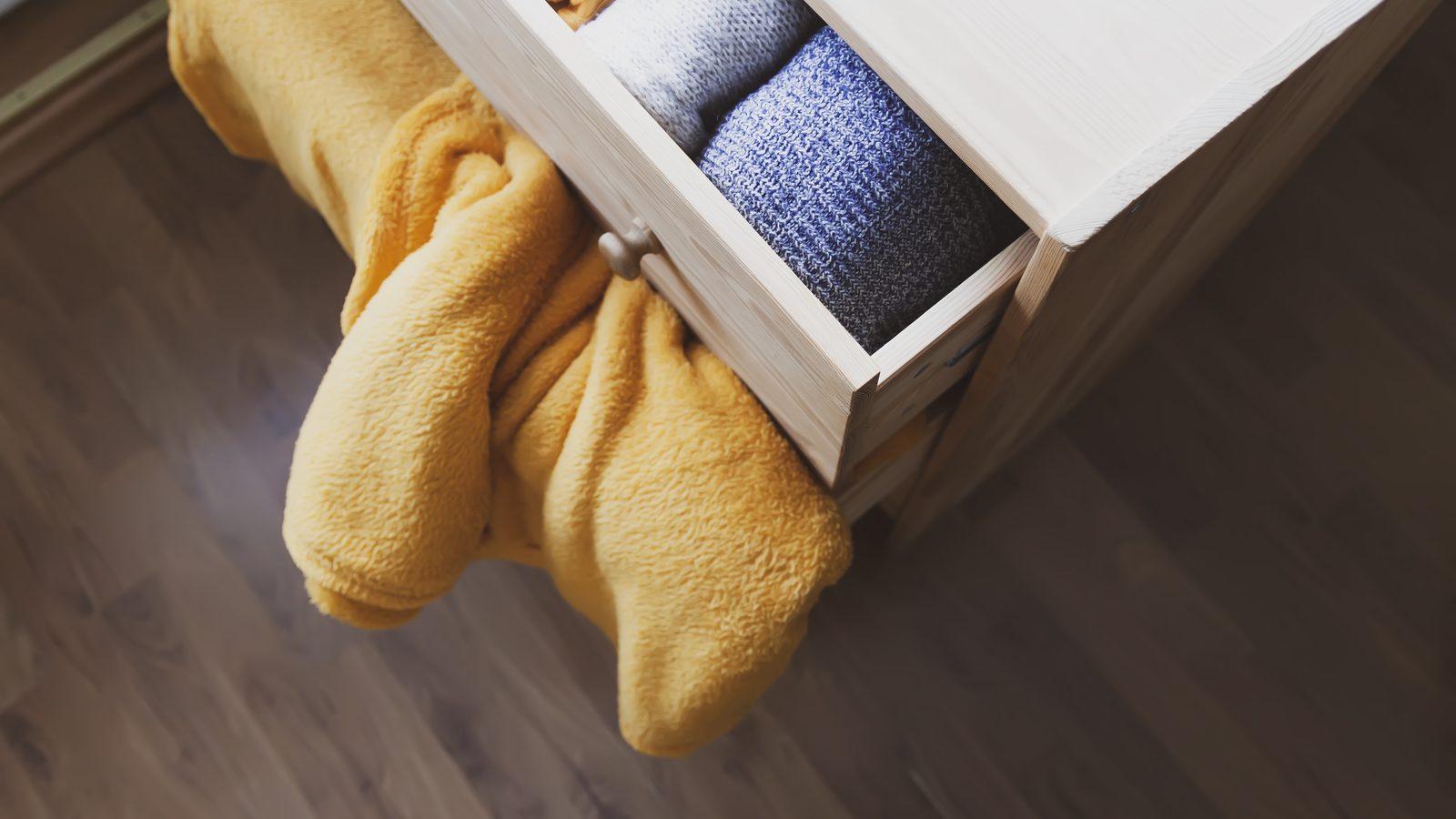 Open wooden dresser drawer with neatly folded knitted clothes inside