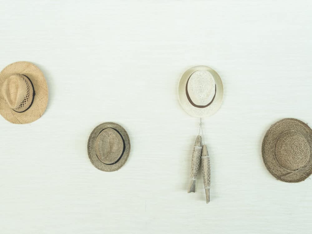Several structured hats hanging by their crowns from a row of wall-mounted hooks, keeping each brim free and uncrushed