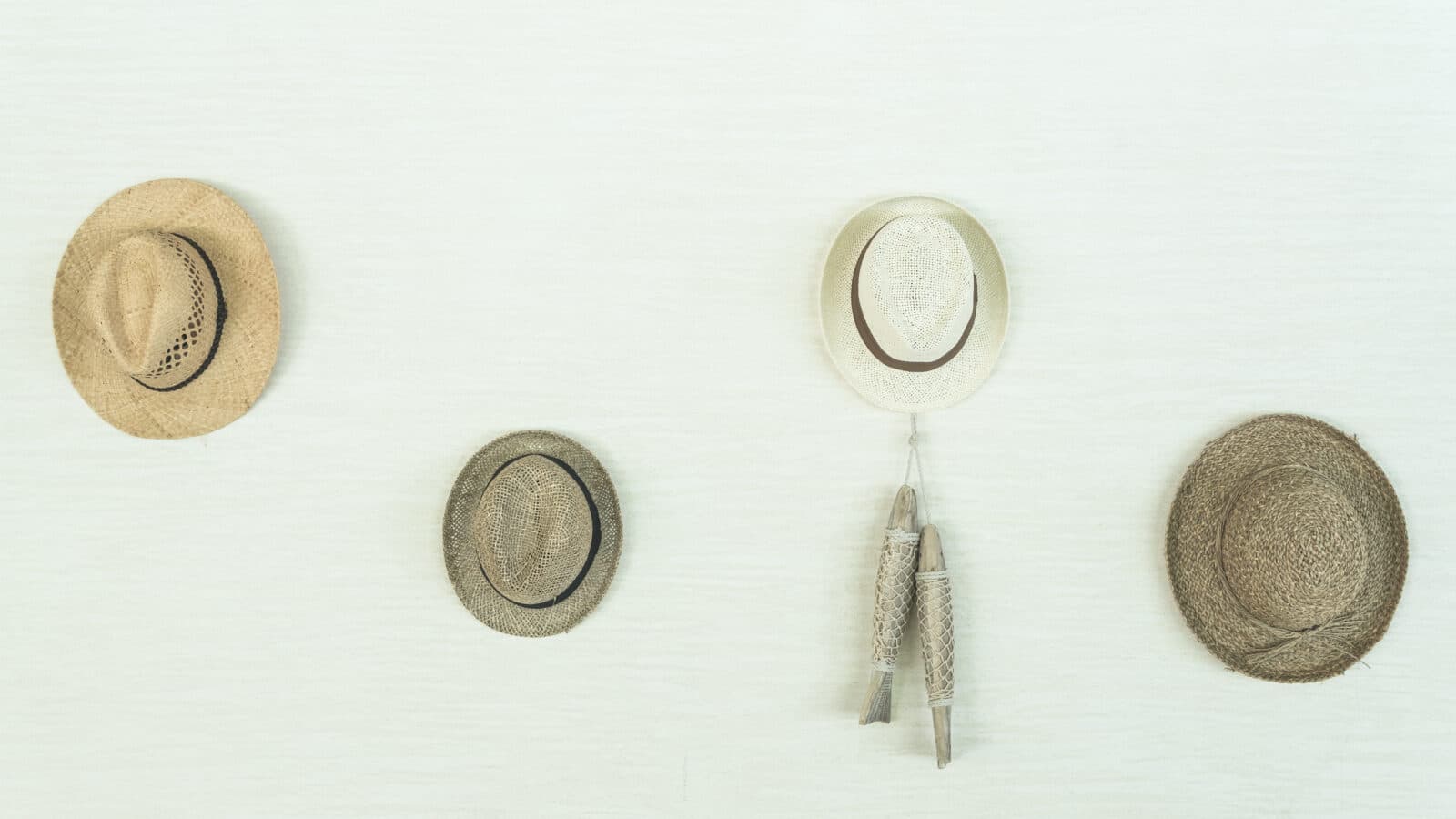 Several structured hats hanging by their crowns from a row of wall-mounted hooks, keeping each brim free and uncrushed
