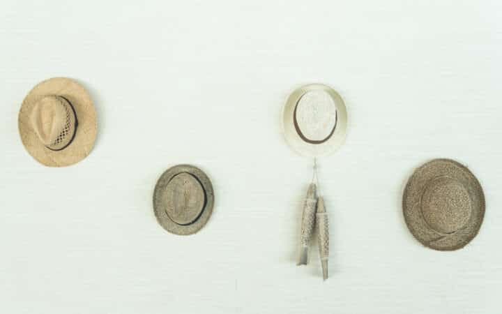 Several structured hats hanging by their crowns from a row of wall-mounted hooks, keeping each brim free and uncrushed