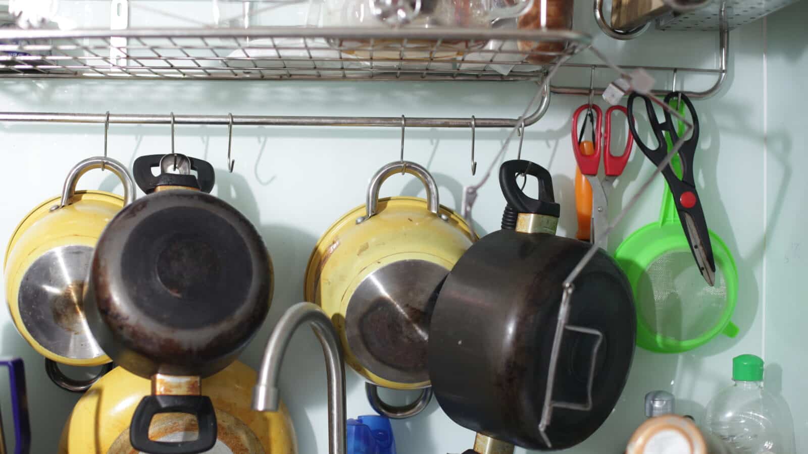 Copper and steel cooking pots and pans hanging from a wall-mounted rail in a kitchen
