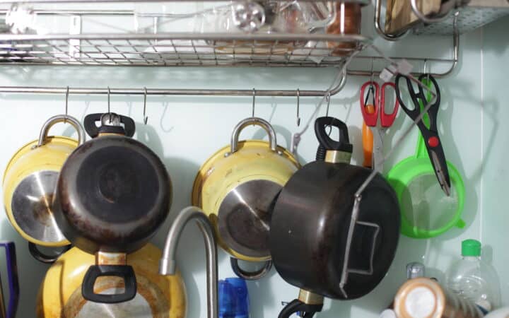 Copper and steel cooking pots and pans hanging from a wall-mounted rail in a kitchen